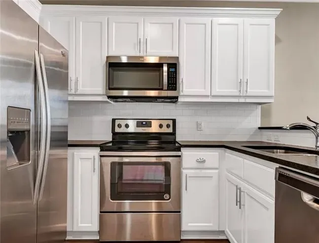 a kitchen with stainless steel appliances granite countertop white cabinets a microwave a sink and a refrigerator