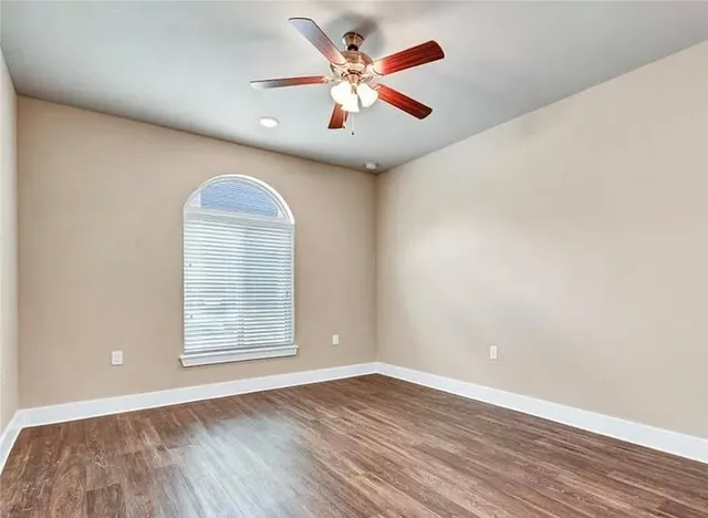 an empty room with wooden floor chandelier fan and windows