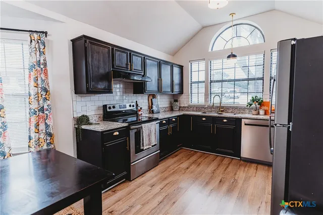 a kitchen with stainless steel appliances granite countertop a stove a sink dishwasher and a refrigerator with wooden floor