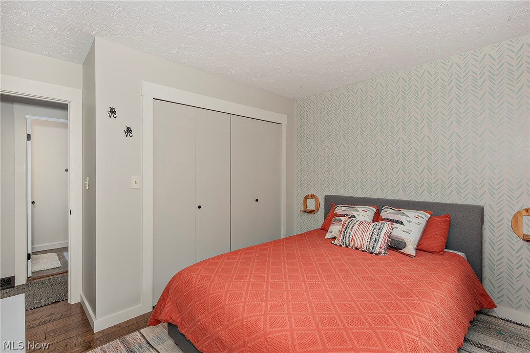 11292 Butternut Road Chardon, OH 44024 - Photo 31 of 49 Bedroom featuring a patterned accent wall, light gray walls, wood-finish flooring, and a large bi-fold closet