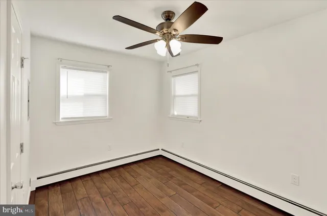 an empty room with wooden floor fan and windows