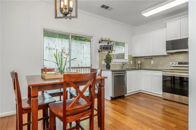 a kitchen with stainless steel appliances granite countertop a stove top oven a sink dishwasher a dining table and chairs with wooden floor