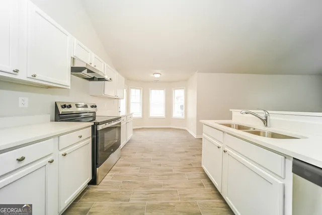 a large white kitchen with granite countertop a sink and dishwasher a stove with wooden floors