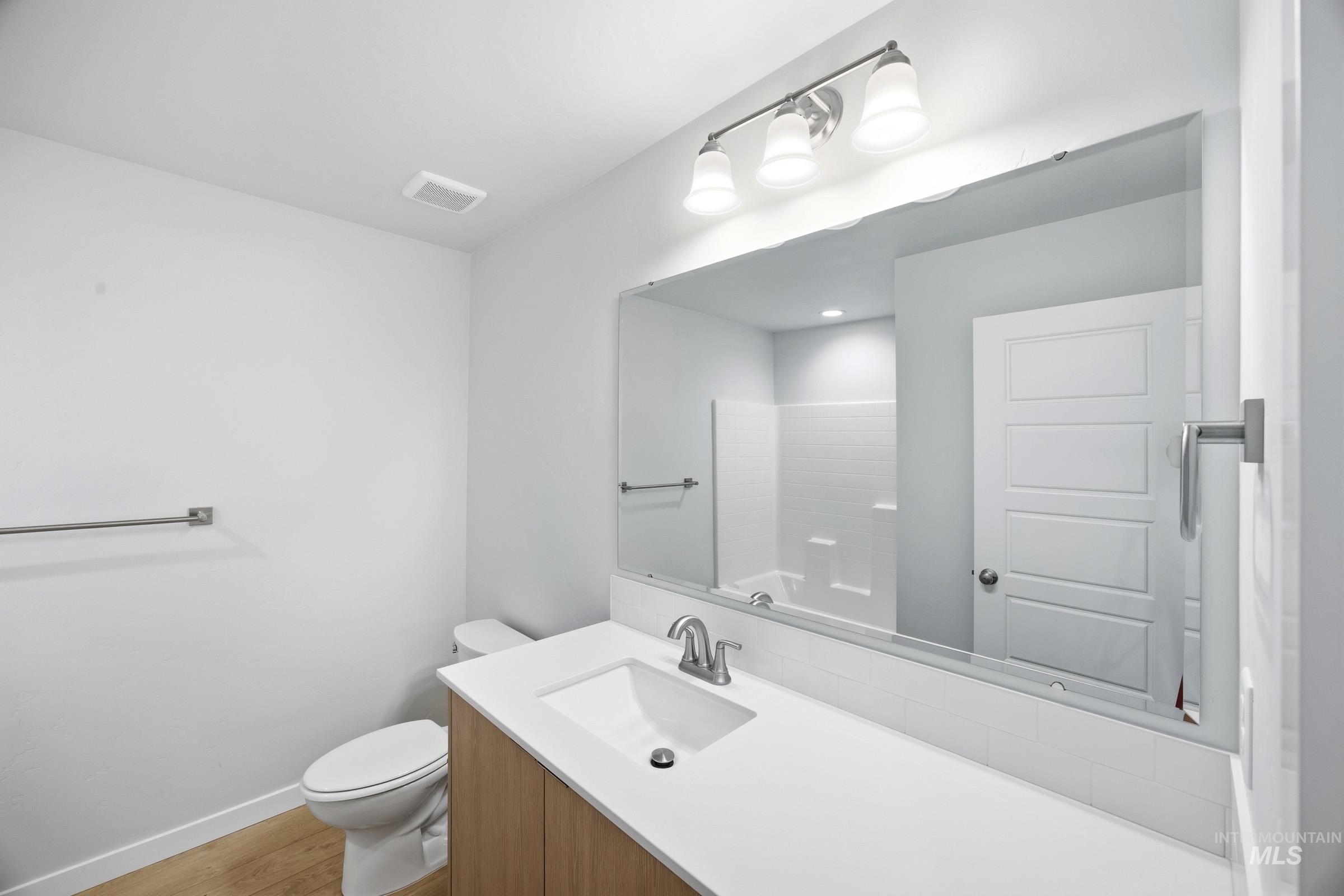 16211 Andes Avenue Caldwell, ID 83607 - Photo 17 of 22 White wall paint, wood-finish flooring, undermount sink, brushed nickel faucet, and a large vanity mirror