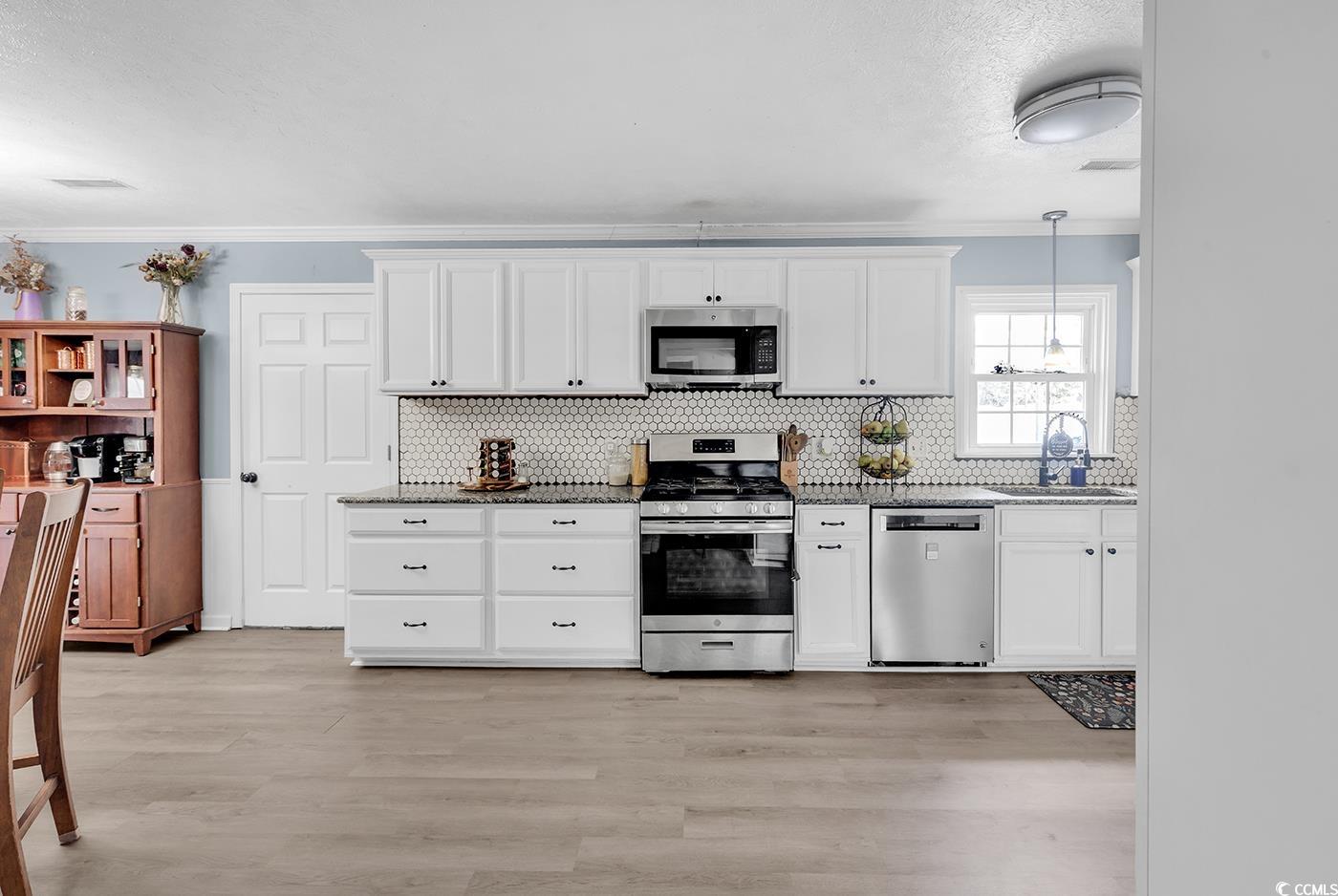 4 Plantation Road Myrtle Beach, SC 29588 - Photo 11 of 40 Kitchen featuring stainless steel appliances, ornamental molding, white cabinets, light wood finished floors, and hanging light fixtures