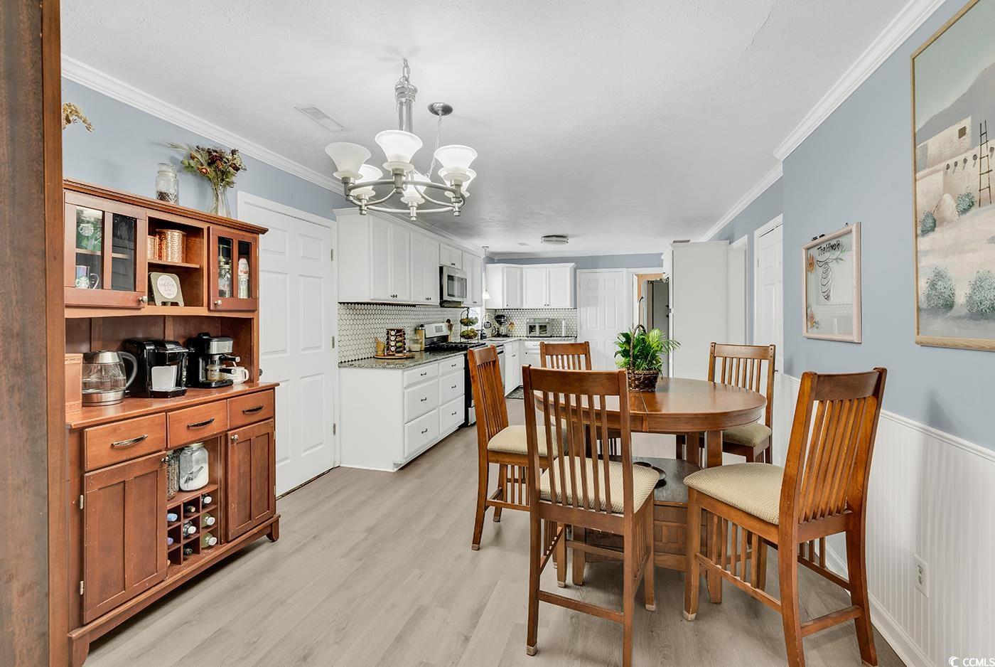 4 Plantation Road Myrtle Beach, SC 29588 - Photo 9 of 40 Dining room with ornamental molding, light wood-style floors, a chandelier, and a wainscoted wall