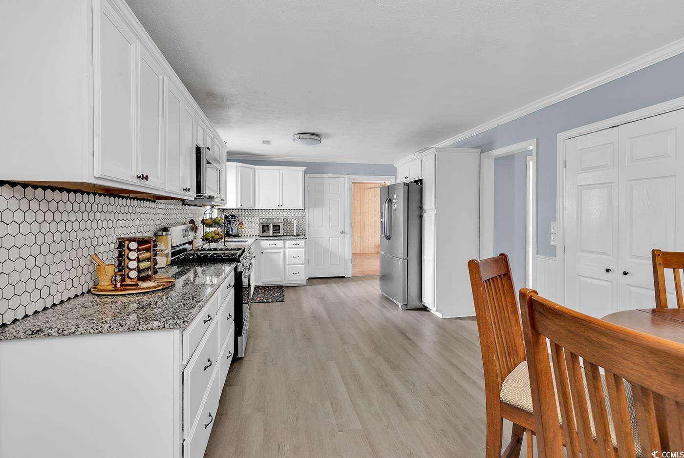 4 Plantation Road Myrtle Beach, SC 29588 - Photo 10 of 40 Kitchen featuring stainless steel appliances, light stone counters, light wood finished floors, white cabinetry, and decorative backsplash