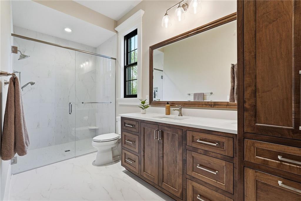 225 Stoup Road Mars, PA 16046 - Photo 26 of 50 The main level en-suite features a walk-in glass shower with ceramic tile surround, dark wood vanity with quartz countertop, a framed mirror, and matching ceramic tile flooring — a well-appointed private bath serving the main level bedroom.