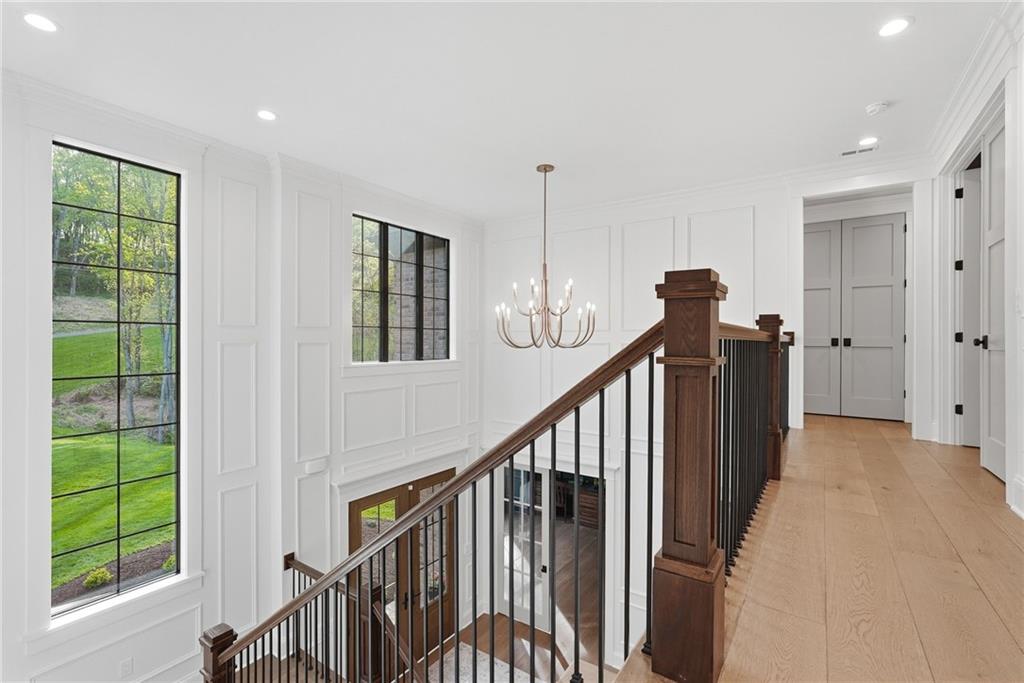 225 Stoup Road Mars, PA 16046 - Photo 27 of 50 The upper level landing continues the craftsmanship of the entry below — poplar wood wainscoting, dark wood staircase with black iron balusters and stair riser lighting, a statement chandelier, and oversized black-framed windows overlooking the manicured grounds. 9-inch engineered white oak hardwood floors carry throughout.