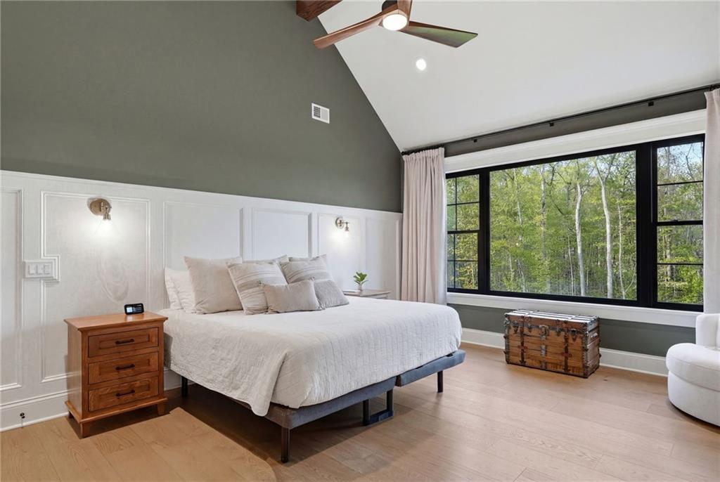 225 Stoup Road Mars, PA 16046 - Photo 29 of 50 The primary suite features a cathedral beamed ceiling with exposed wood beams, poplar wood wainscoting, a floor-to-ceiling stone electric fireplace with a wood mantel, wall sconces, recessed lighting, a ceiling fan, and floor-to-ceiling black-framed windows with sweeping wooded views. 9-inch engineered white oak hardwood floors run throughout, and the door leads directly to the primary bath and walk-in closet.