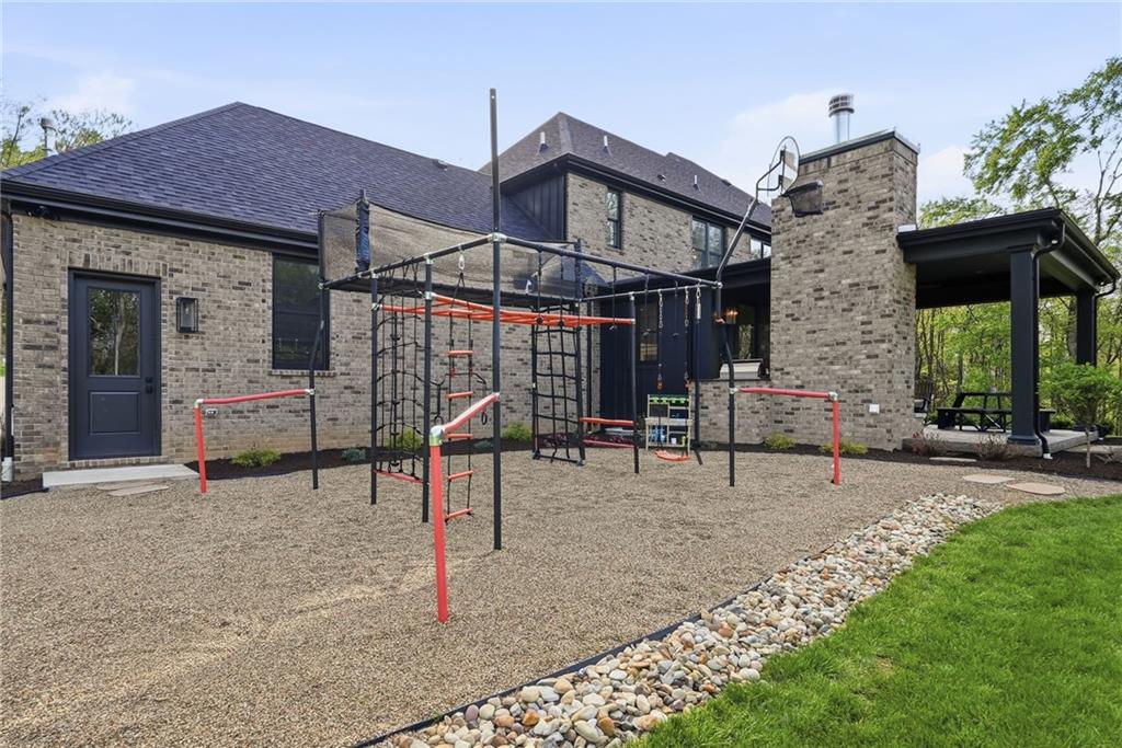225 Stoup Road Mars, PA 16046 - Photo 45 of 50 The backyard offers something for everyone — a large play structure with a gravel base sits just off the walk-out lower level, with the covered patio, brick fireplace, and built-in Wolf gas grill visible to the right, all set against the private wooded backdrop of 6.45 acres.