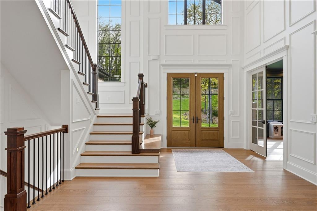 225 Stoup Road Mars, PA 16046 - Photo 8 of 50 The two-story entry sets the tone immediately — floor-to-ceiling poplar wood wainscoting, soaring windows flooding the space with natural light, 9-inch engineered white oak hardwood floors, a built-in bench, and a staircase with dark wood treads and black iron balusters. The glass doors to the right lead to the private paneled office.