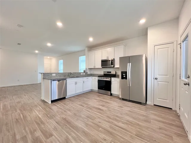 a large kitchen with stainless steel appliances granite countertop a stove a sink dishwasher a refrigerator and white cabinets with wooden floor