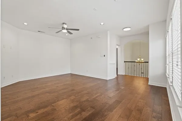 an empty room with wooden floor ceiling fan and windows