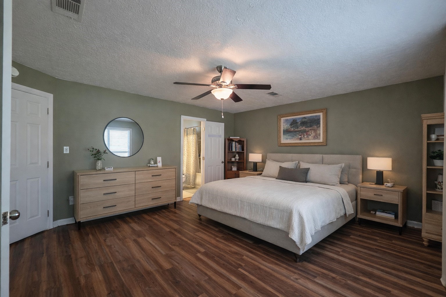 145 Cypress Road Livingston, TX 77351 - Photo 4 of 16 Spacious bedroom with warm wood flooring, a ceiling fan, and soft green walls. It includes a large bed, vintage-style dresser with mirrors, bedside tables, and a cozy reading nook. Natural light enhances the inviting atmosphere.