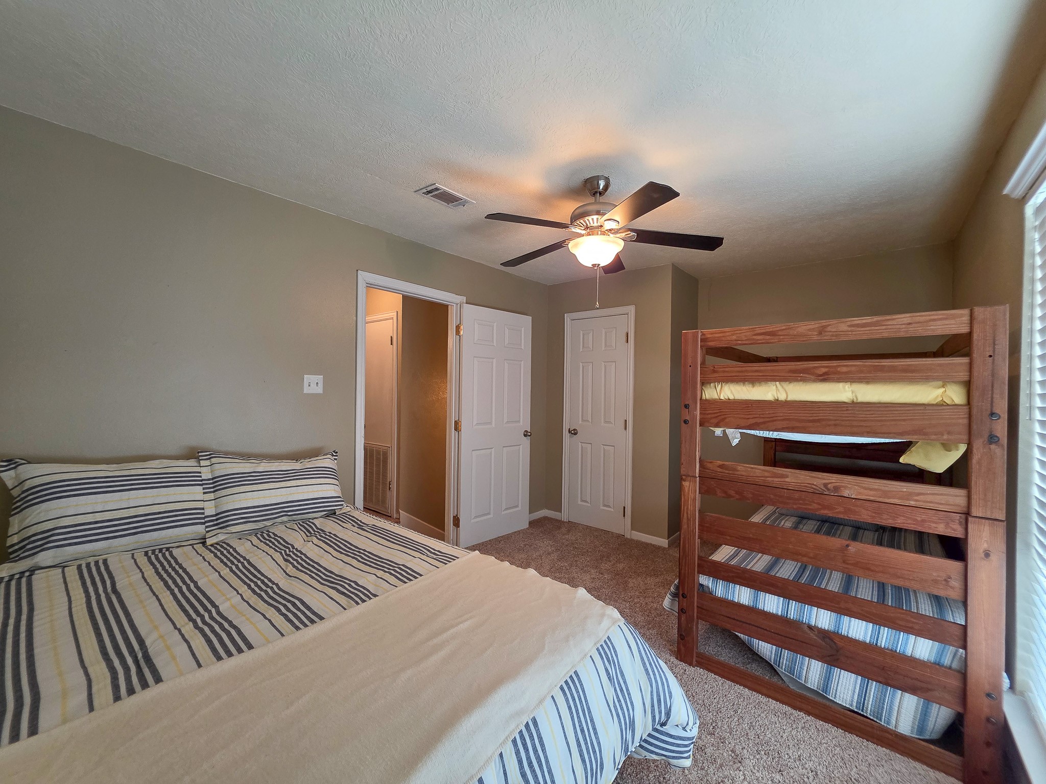145 Cypress Road Livingston, TX 77351 - Photo 8 of 16 This is a cozy bedroom featuring a double bed, a set of wooden bunk beds, carpeted flooring, and a ceiling fan. The room has neutral walls and ample natural light from the window. This allows for lots of heads in beds which is an investors asset.