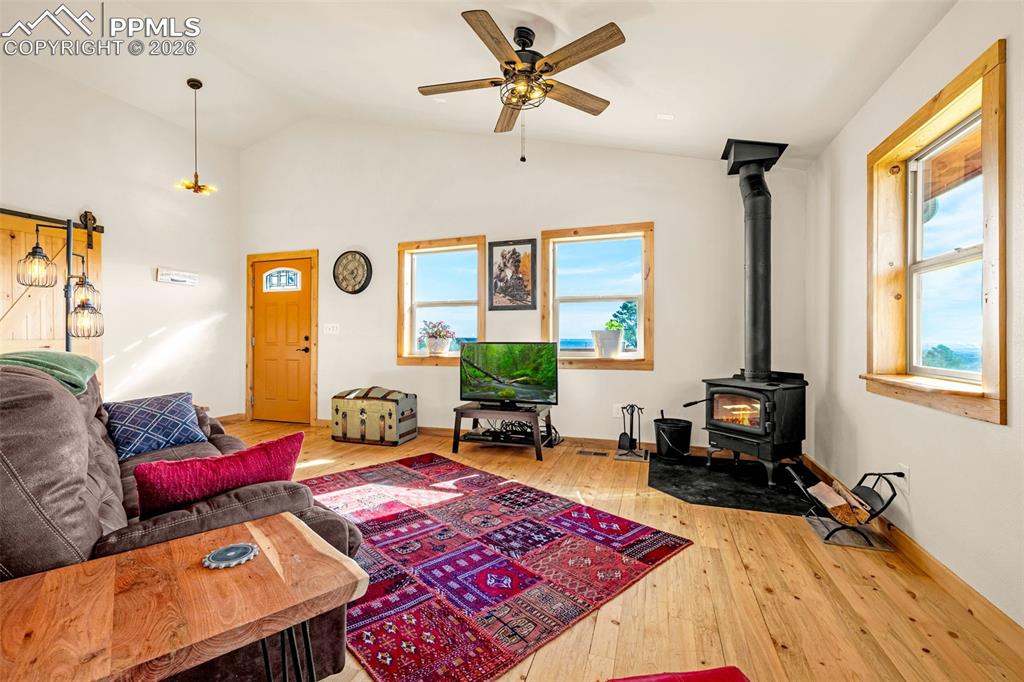 8480 Delaware Road Colorado Springs, CO 80926 - Photo 5 of 49 Living area featuring a wood stove, light wood finished floors, lofted ceiling, and ceiling fan