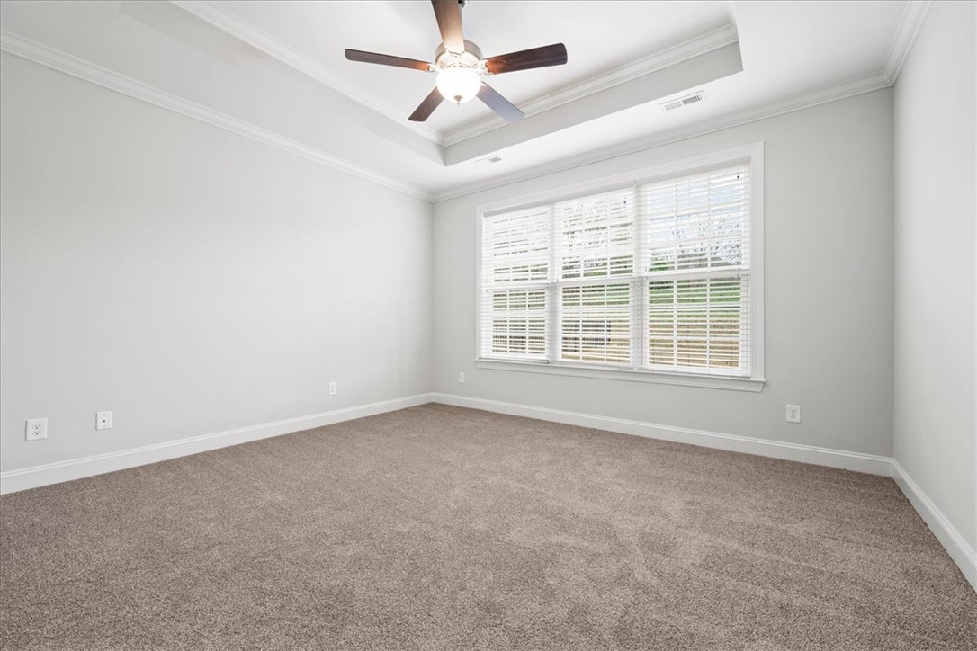 102 Ripplestone Way Anderson, SC 29621 - Photo 19 of 39 A spacious primary bedroom featuring plush carpeting, a large window, and a stylish ceiling fan with tray ceiling.