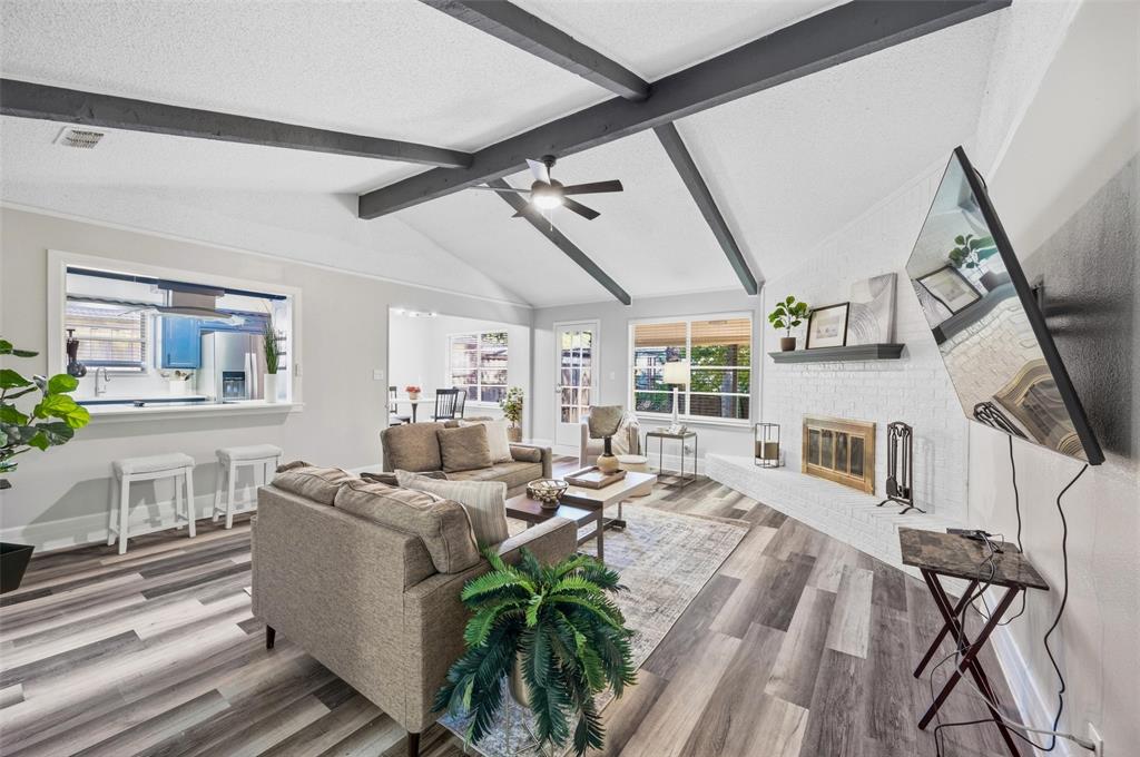 608 Ridgewood Circle Hurst, TX 76054 - Photo 7 of 38 Vaulted ceiling with exposed beams, wood-finish flooring, white brick fireplace with a mantel, and a kitchen pass-through window