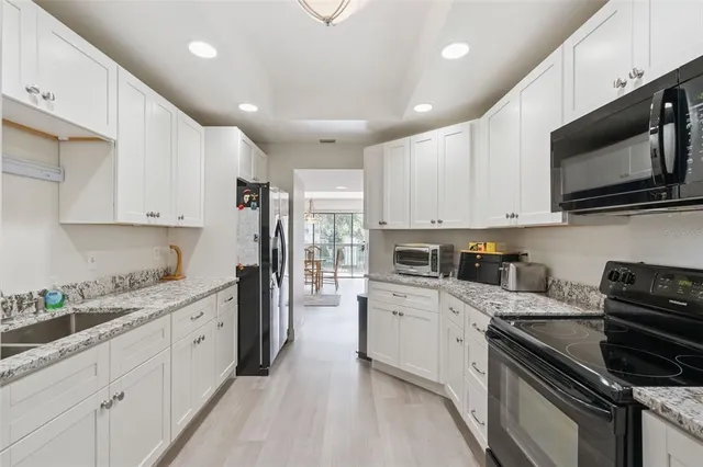 a kitchen with stainless steel appliances granite countertop grey cabinets a stove a sink and a refrigerator