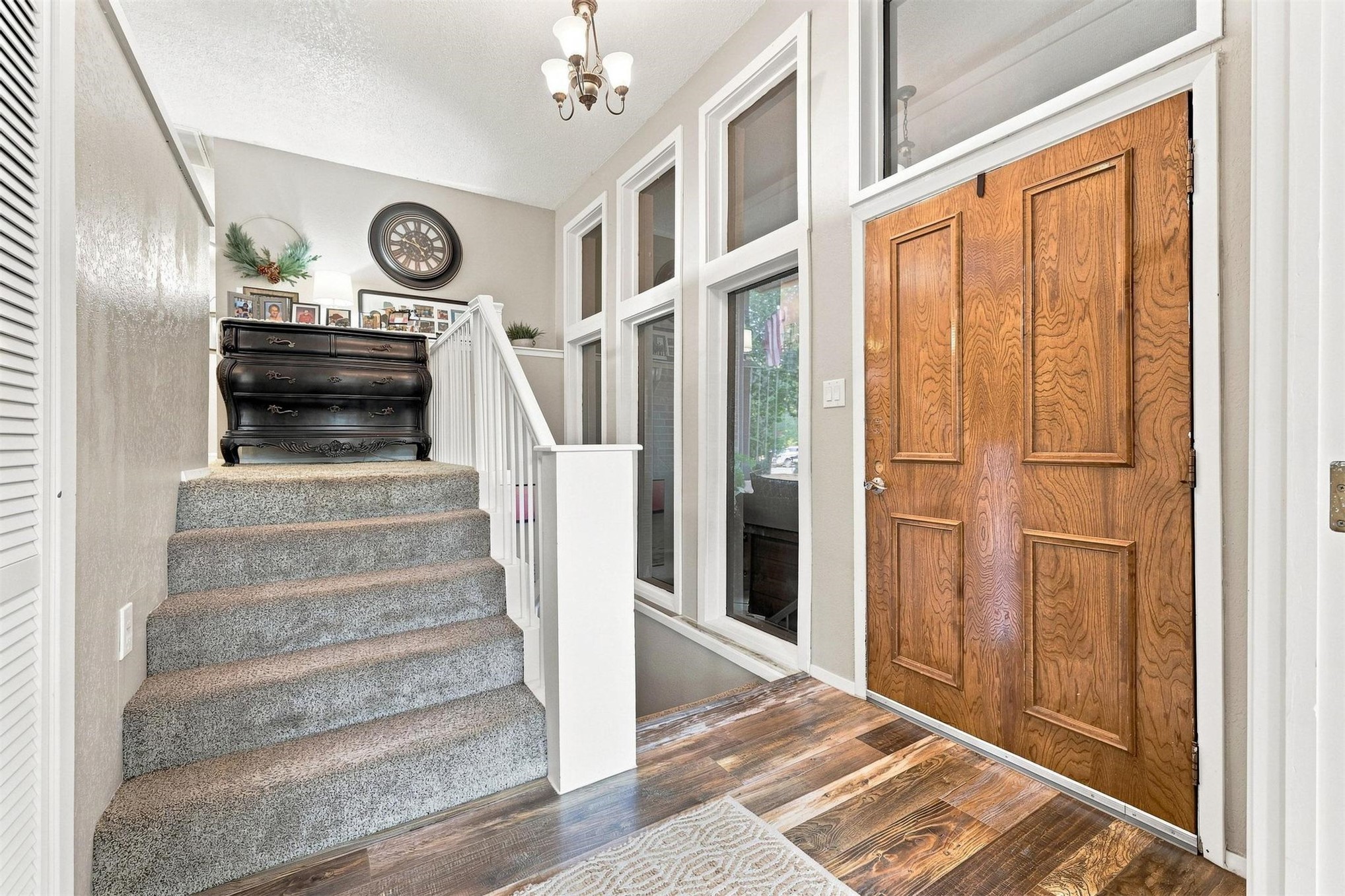 Wood-finish flooring, paneled entry door with transom window, multiple sidelight windows, and carpeted stairs with white railing