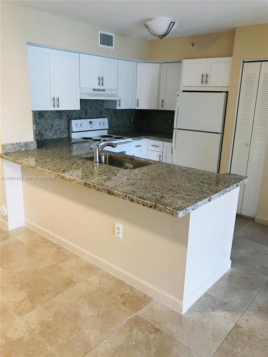 2031 Renaissance Boulevard, Unit 106 Miramar, FL 33025 - Photo 16 of 19 a kitchen with granite countertop a sink a stove a refrigerator a white stove top oven and white cabinets