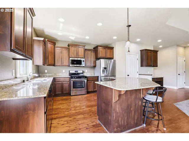 a kitchen with stainless steel appliances kitchen island granite countertop a sink refrigerator and cabinets