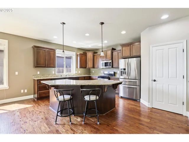 a kitchen with stainless steel appliances kitchen island granite countertop a table chairs sink and refrigerator