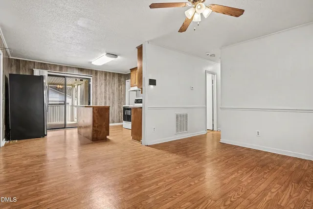 a view of a livingroom with wooden floor and a kitchen space with a refrigerator