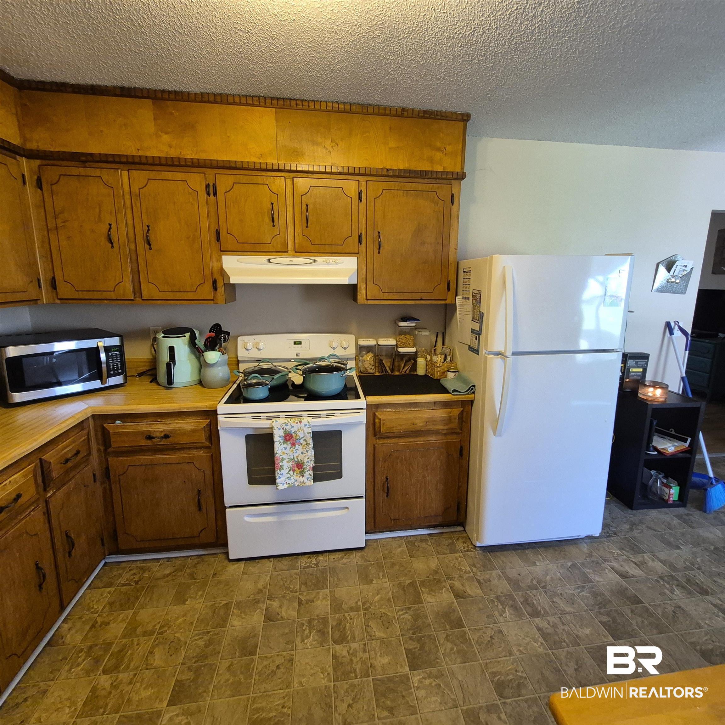 721 Perryman Street Evergreen, AL 36401 - Photo 10 of 26 Kitchen featuring white appliances, wood finish cabinetry, stone finish flooring, and a textured ceiling