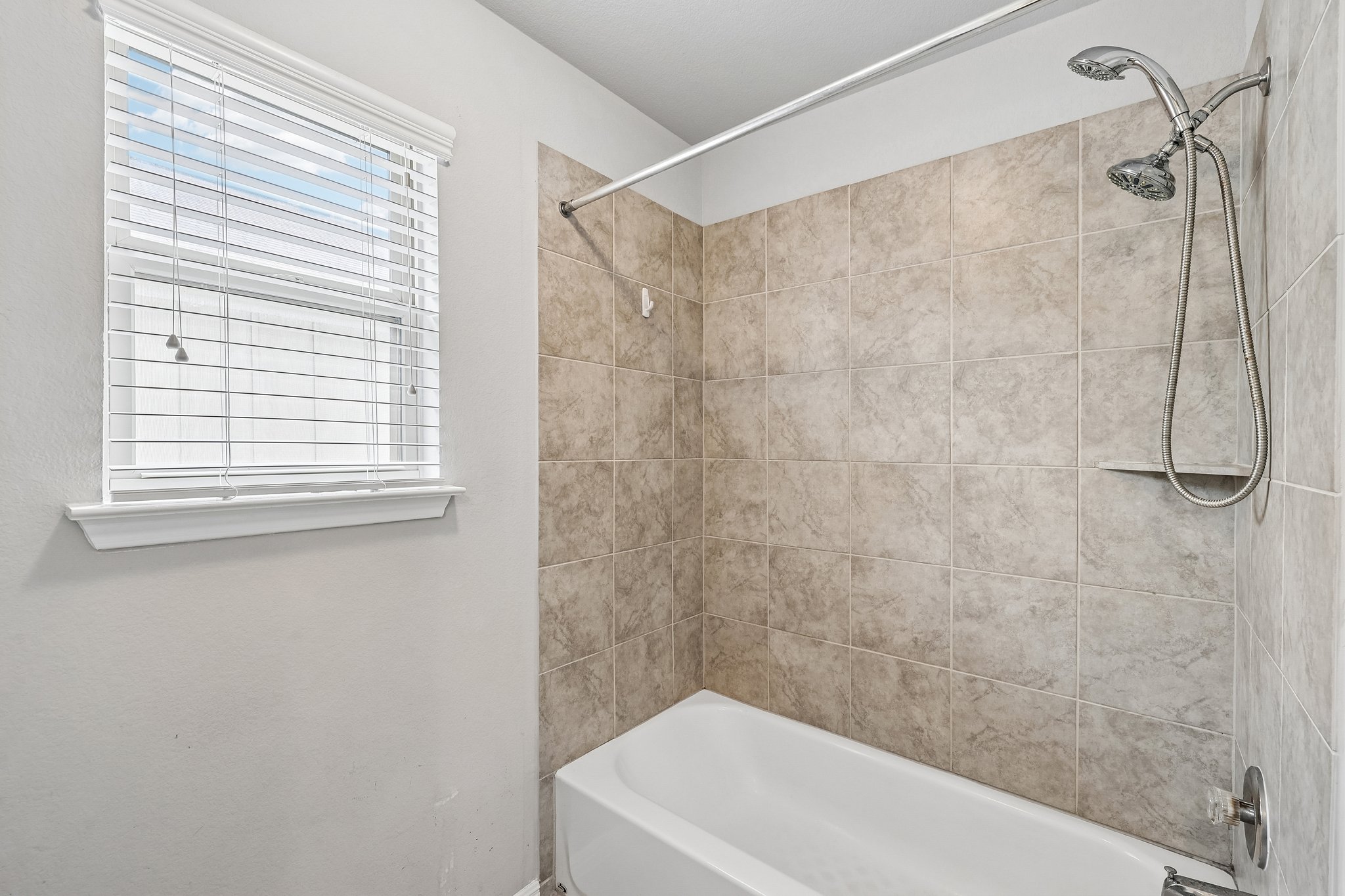 387 Guemal Road Buda, TX 78610 - Photo 23 of 39 Bathtub with a tiled surround featuring a built-in shower niche, dual shower heads, and chrome fixtures