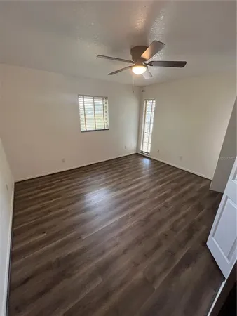 an empty room with wooden floor fan and windows