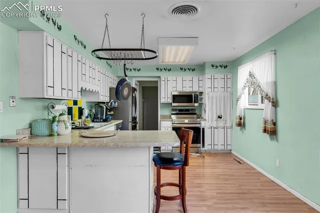 a kitchen with stainless steel appliances a stove a refrigerator a oven a sink a dining table and chairs with wooden floor