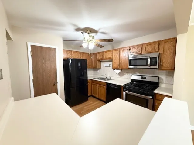 a kitchen with stainless steel appliances kitchen island granite countertop a refrigerator a sink dishwasher a stove and black cabinets with wooden floor