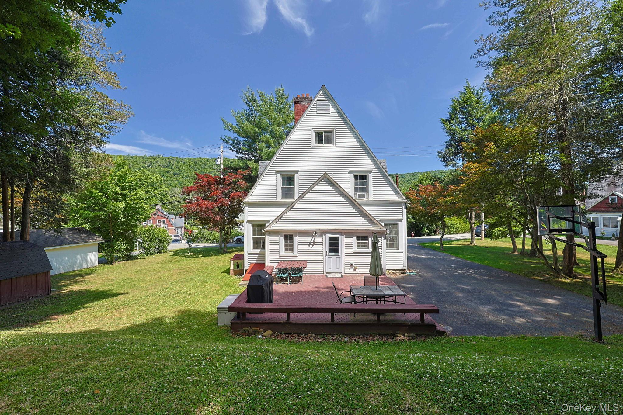 9 Library Road Tuxedo Park, NY 10987 - Photo 32 of 37 Rear exterior with a spacious wood-finish deck, white siding, and a prominent red brick chimney