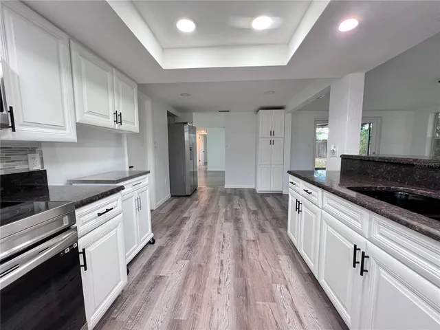 a large kitchen with granite countertop a large stove top oven a sink dishwasher and white cabinets with wooden floor