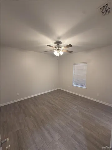 an empty room with wooden floor ceiling fan and window
