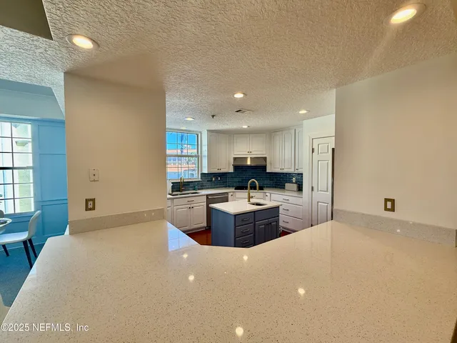 a large kitchen with a large counter top a sink stainless steel appliances and cabinets