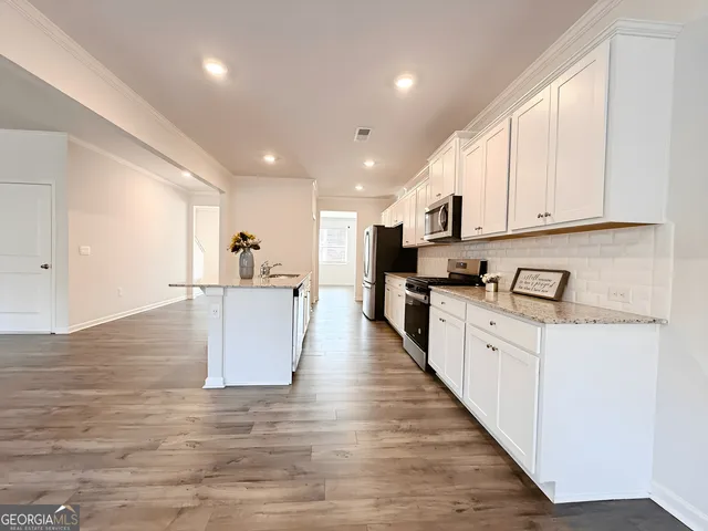 a kitchen with stainless steel appliances granite countertop a stove a sink a refrigerator and white cabinets with wooden floor