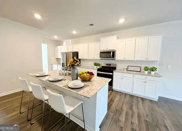 a kitchen with a sink a stove a kitchen island with chairs and white cabinets