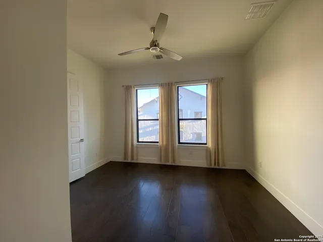 an empty room with wooden floor fan and windows
