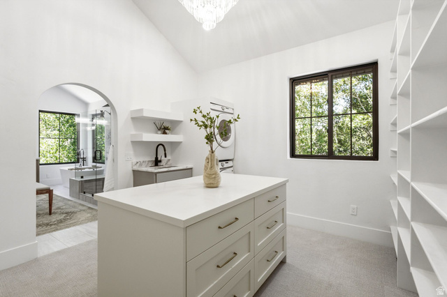 3027 Homestead Road Park City, UT 84098 - Photo 32 of 62 Spacious dressing room featuring a central island with drawers, extensive built-in shelving, a laundry area with stacked appliances, and an arched entry to a bathroom with a freestanding tub
