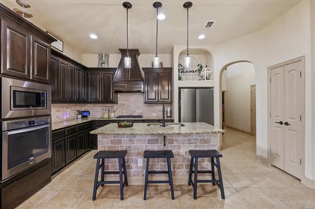 a kitchen with stainless steel appliances granite countertop a stove a refrigerator a kitchen island a sink and a wooden cabinets