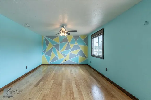 a view of an empty room with window and chandelier fan