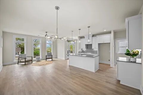 a large white kitchen with kitchen island a stove a sink a refrigerator white cabinets and couches with wooden floor