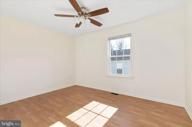 an empty room with wooden floor fan and windows