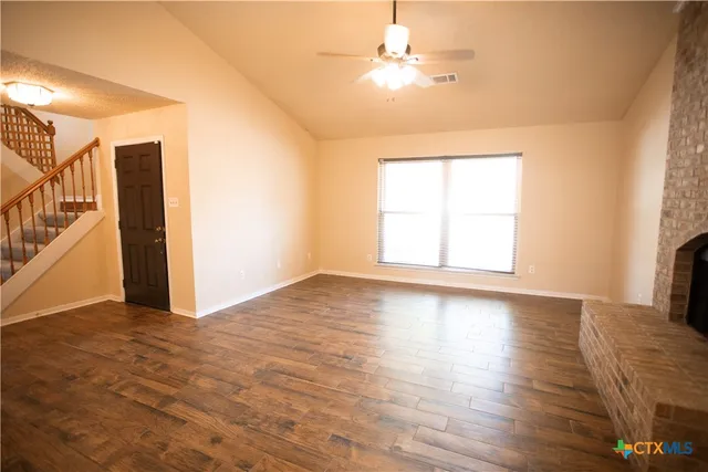 an empty room with wooden floor chandelier fan and windows