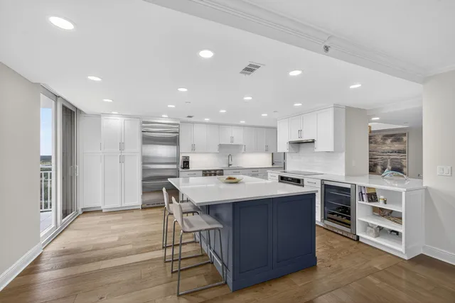 a large kitchen with kitchen island a stove a sink a refrigerator and white cabinets with wooden floor