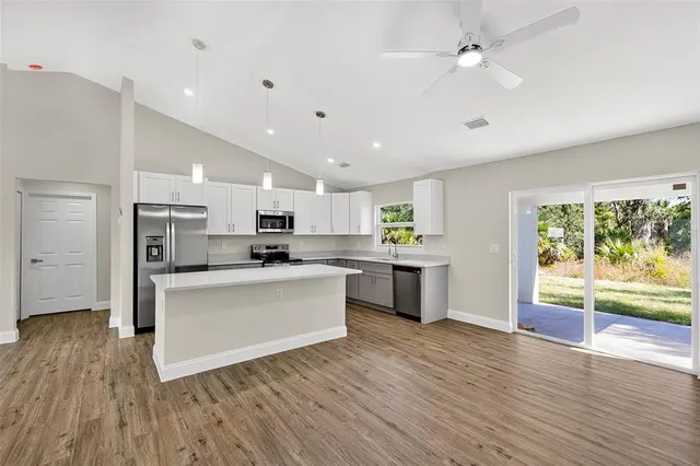 a large kitchen with stainless steel appliances granite countertop a stove top oven a sink dishwasher and white cabinets with wooden floor