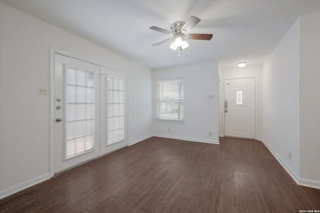 an empty room with wooden floor chandelier fan and windows